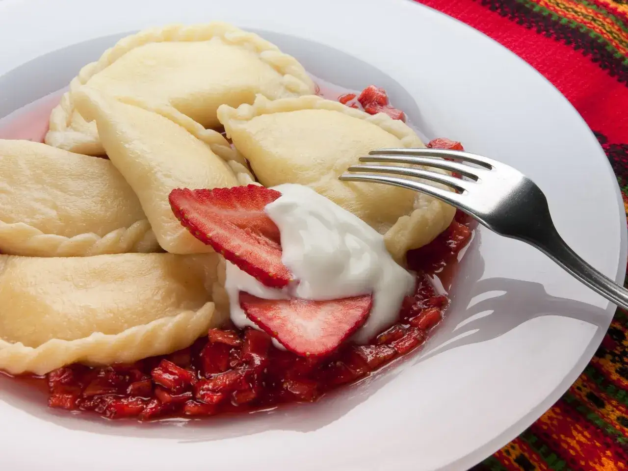 Pyszne pierogi z serem, podane z truskawkami i śmietaną, jak z przepisu na pierogi z serem Magdy Gessler.