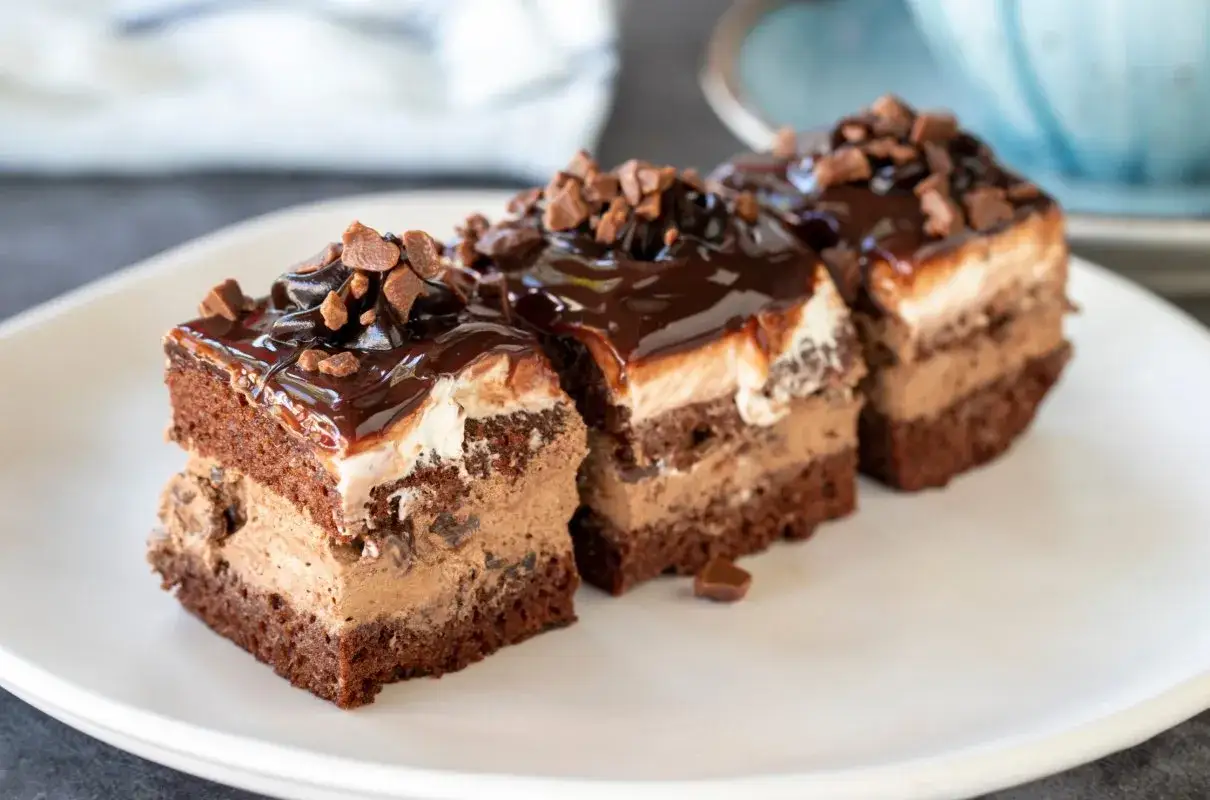 Trzy kawałki ciasta kinder bueno z mascarpone, polane czekoladą i posypane wiórkami.
