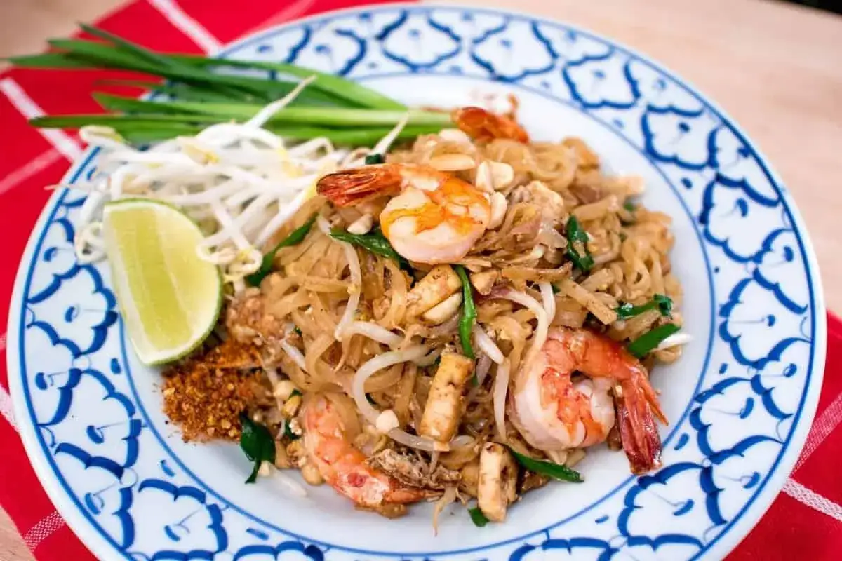 Pad thai co to? Aromatyczny makaron ryżowy z krewetkami, kiełkami i limonką na talerzu.