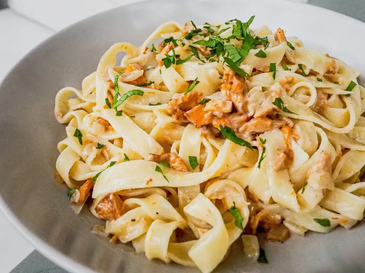 Tagliatelle w kremowym sosie kurkowym, posypane świeżą natką pietruszki. Pyszne danie, które zachwyci każdego miłośnika grzybów.