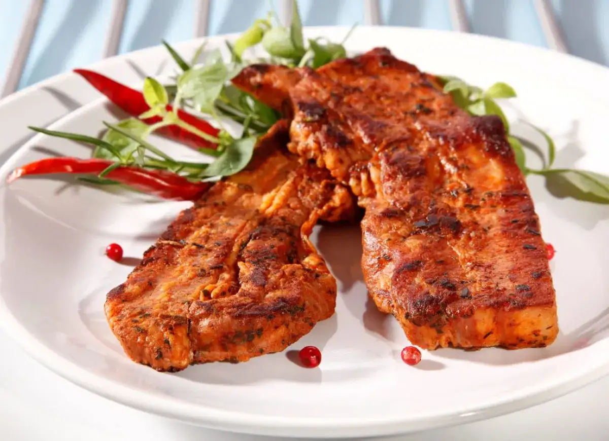 Grillowany boczek w aromatycznej marynacie, ozdobiony papryczkami chili i zielonymi ziołami. Idealny na letnie przyjęcie.
