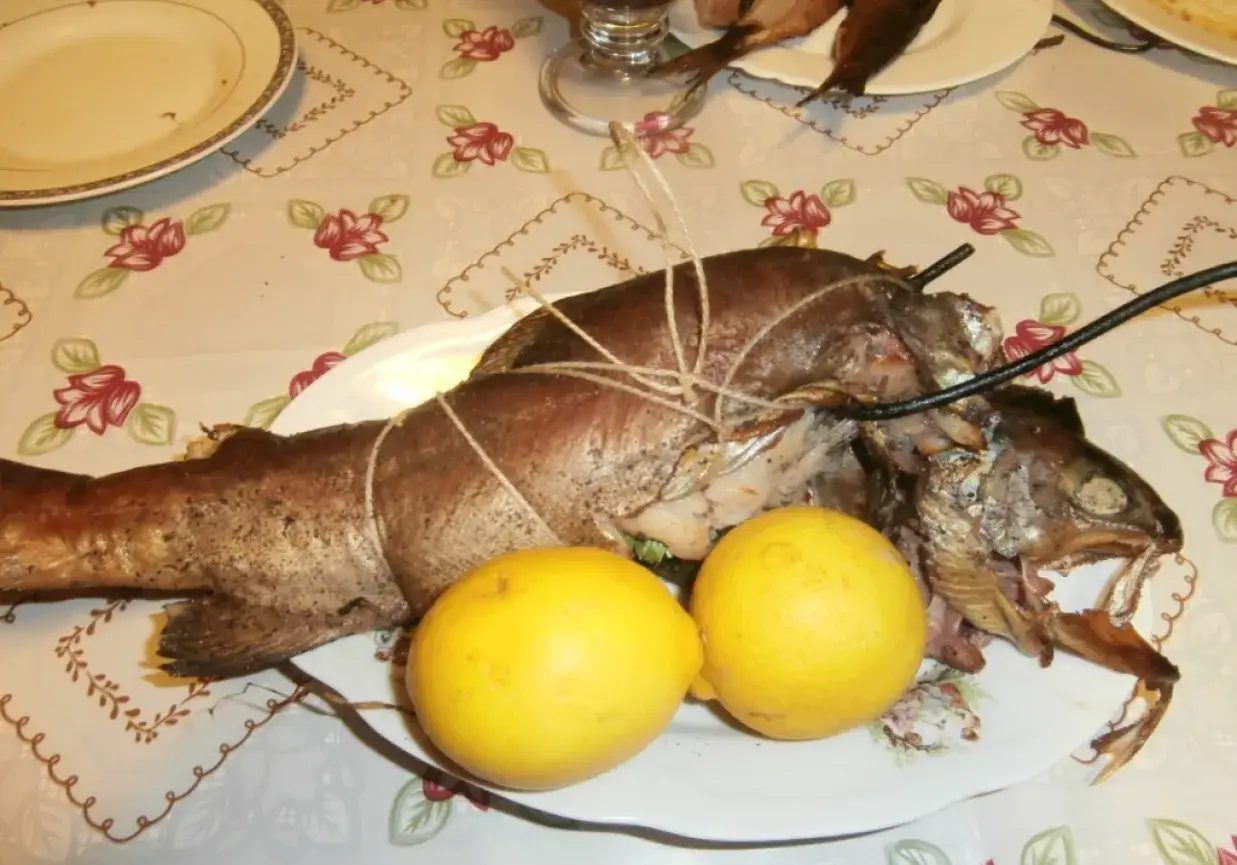 Pstrąg wędzony, związany sznurkiem, leży na talerzu z dwoma cytrynami. Gotowy do podania.