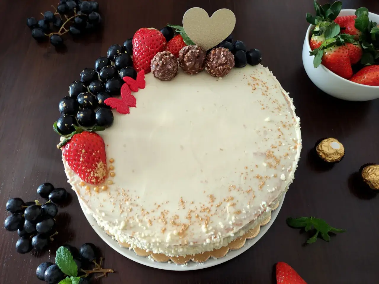 Wyjątkowy tort z kremem mascarpone i białej czekolady, ozdobiony owocami, czekoladkami i złotym sercem.
