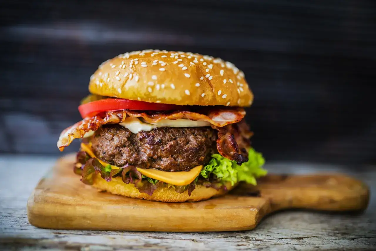 Soczyste mięso na burgery z bekonem, serem i warzywami na desce.