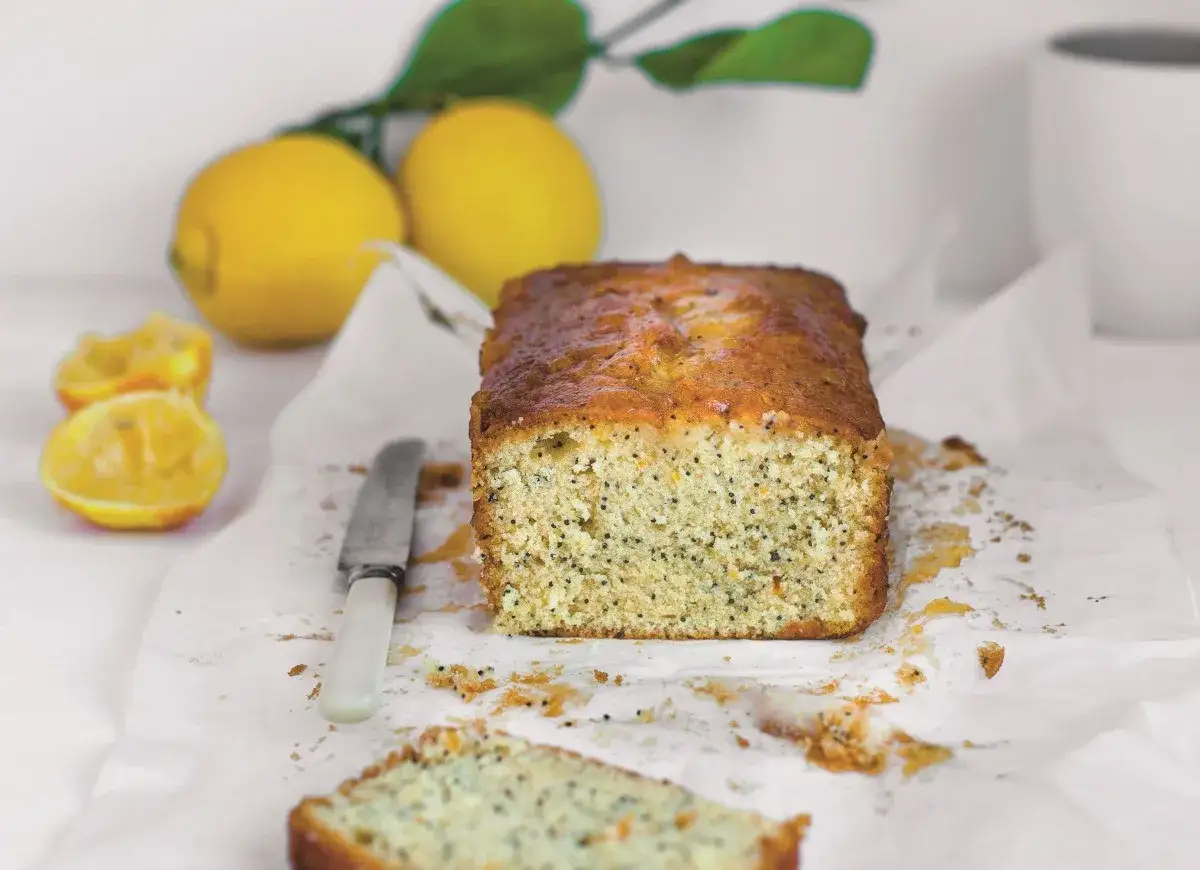 Piegusek ciasto cytrynowe z makiem, lśniące od lukru, obok świeżych cytryn i noża.