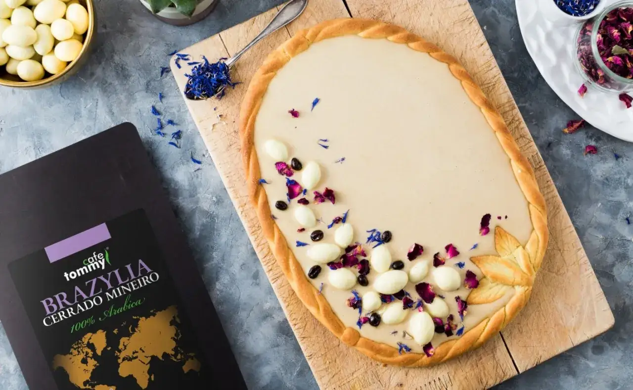 Oryginalny mazurek wielkanocny z kremem kawowym, udekorowany bakaliami i płatkami róż. Obok paczka kawy Tommy Cafe Brazylia.