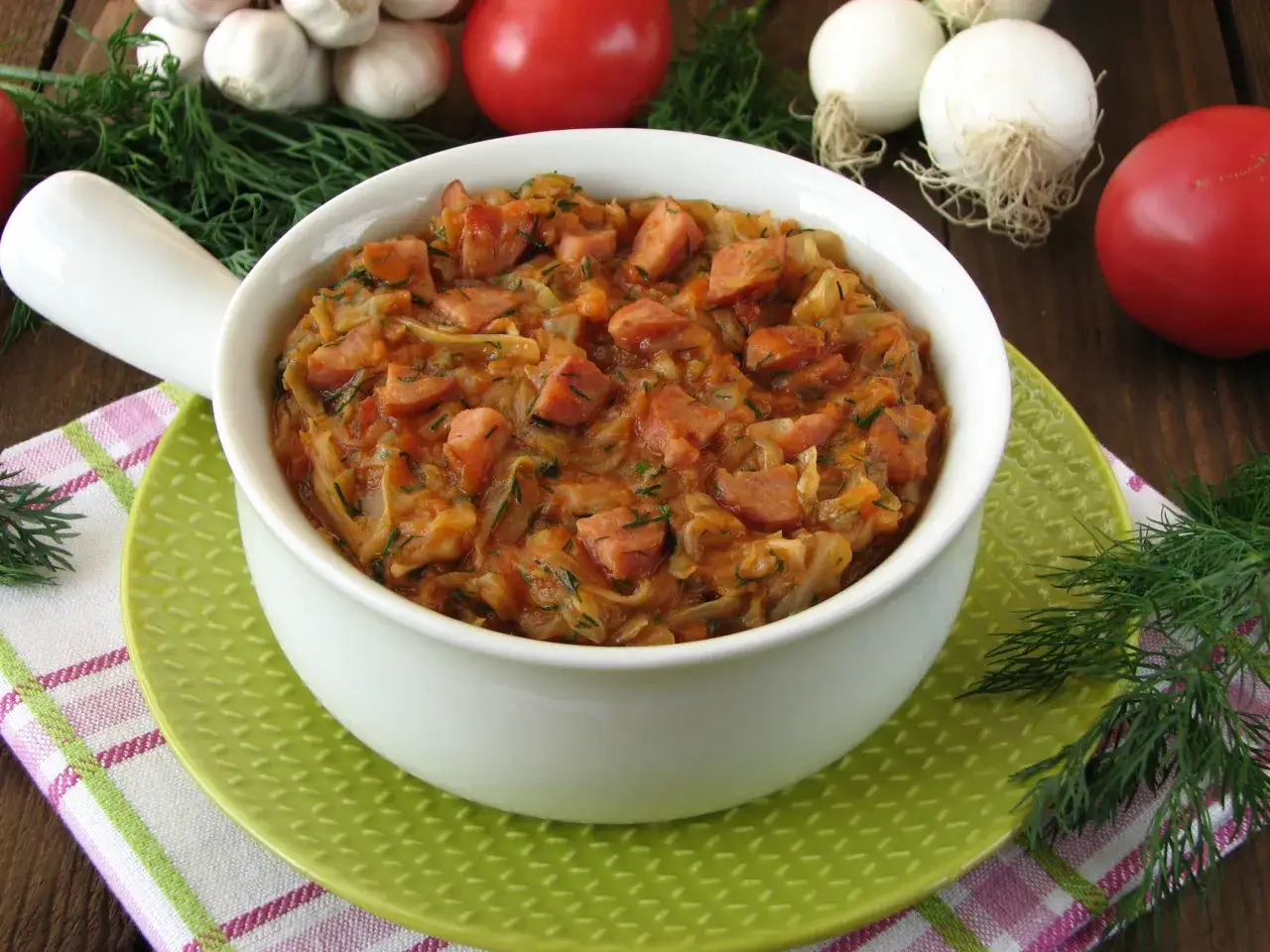 Jak ugotować dobry bigos z młodej kapusty? Aromatyczne danie z kapusty, kiełbasy i pomidorów, ozdobione koperkiem.