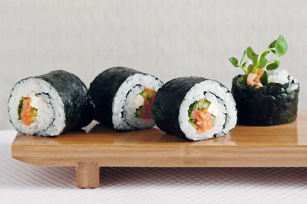 Roladki sushi z łososiem, ogórkiem i serkiem do sushi, udekorowane kiełkami.