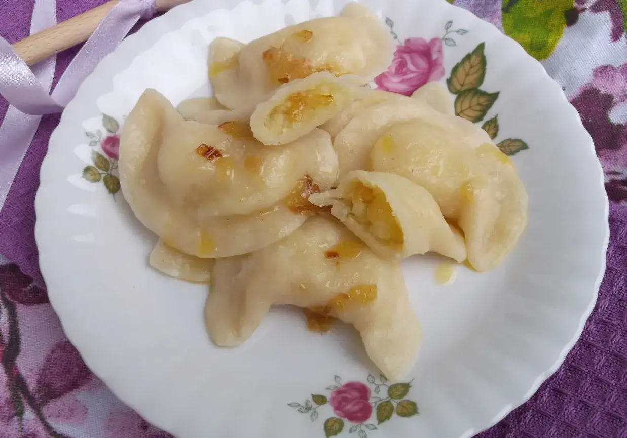 Pyszne pierogi ukraińskie z ziemniakami i cebulką, polane tłuszczem, na talerzu z różami.