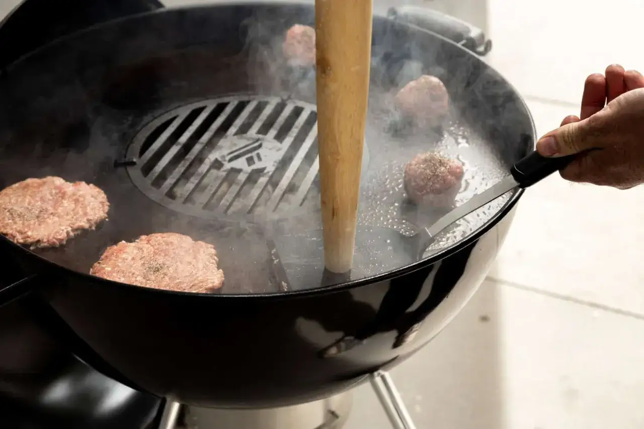 Na grillu powstają soczyste kotlety do burgerów. Widzimy, jak drewniany tłuczek dociska mięso, tworząc idealny smash burger.