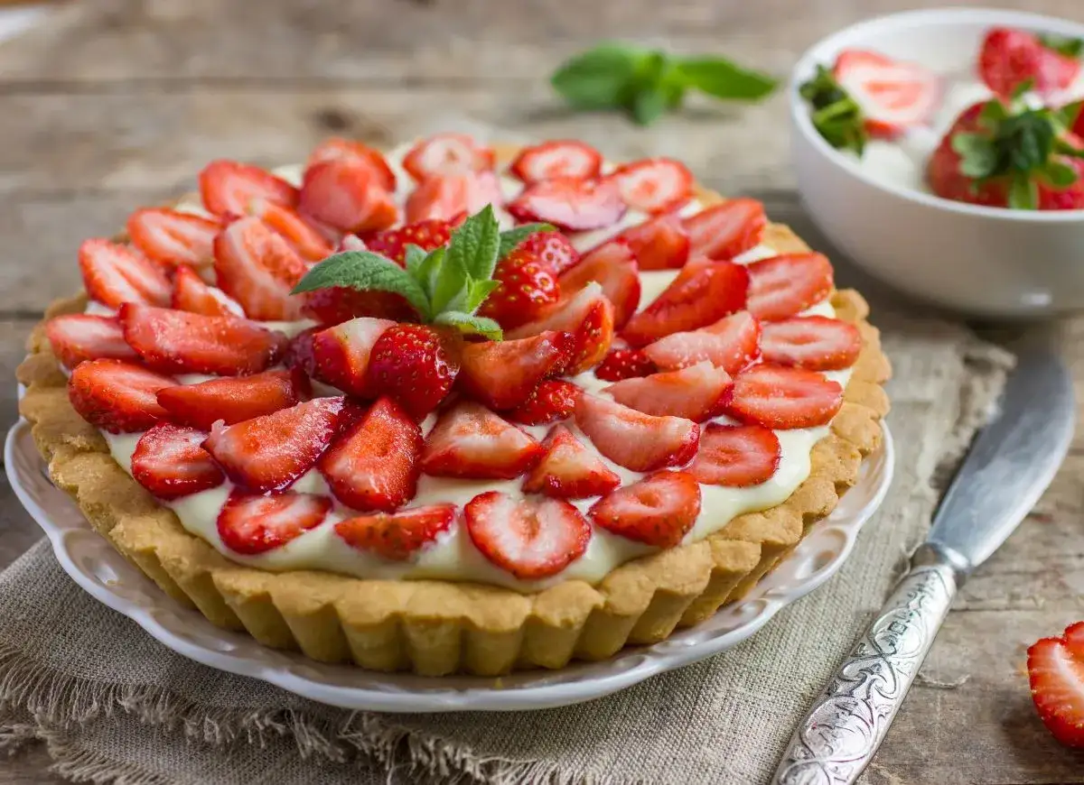 Pyszna tarta z truskawkami i kremem, ozdobiona listkami mięty. Idealna na letnie popołudnie.