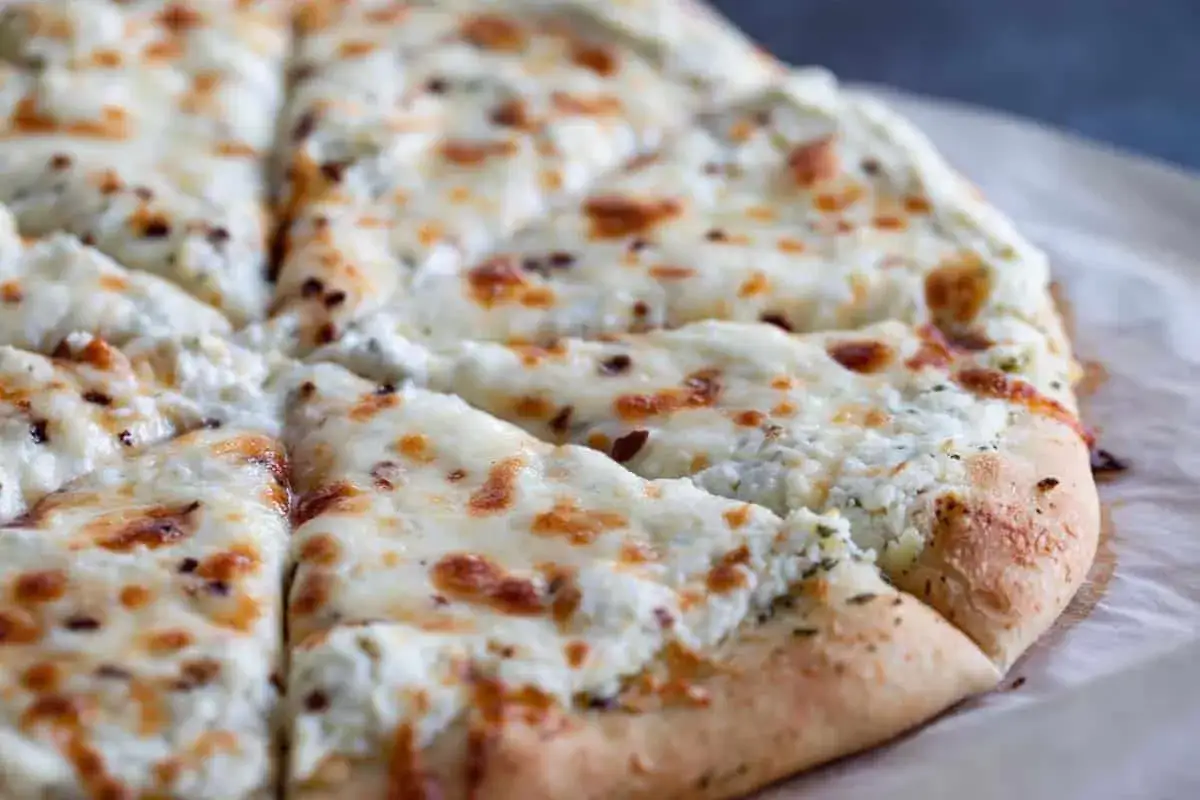Pyszna pizza bianca z kremowym serem i ziołami, pokrojona na kawałki.