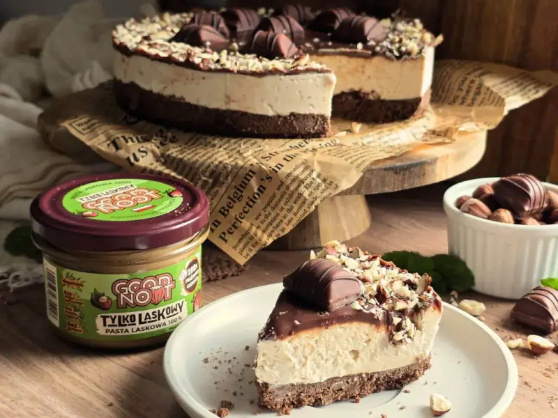 Pyszne ciasto kinder bueno z mascarpone, udekorowane orzechami i kawałkami czekolady. Obok słoik pasty z orzechów laskowych.